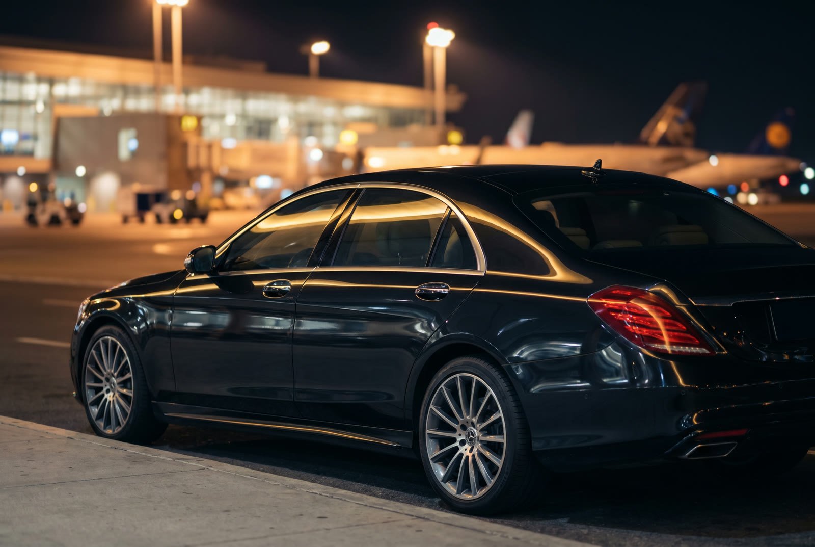 A black sedan on the tarmac at night, ready for an airport pickup
